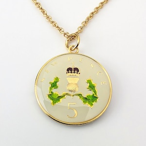May include: A gold chain necklace with a pendant featuring a 5 pence coin from the United Kingdom. The coin has a white background with a gold crown, a thistle, and the number 5. The thistle is surrounded by green leaves.