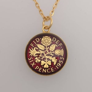 May include: Gold-toned necklace featuring a pendant with a red enamel background. The pendant is a Six Pence coin from 1953, with gold-colored floral and text details. The chain is delicate and gold-colored.