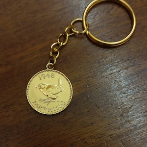 May include: A gold-colored keychain featuring a 1948 British Farthing coin with a wren design. The coin is attached to a gold-colored chain and a circular key ring.