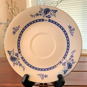 May include: A white saucer with a blue and white floral pattern. The saucer has a silver rim and a diamond pattern around the edge.