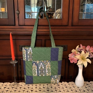 May include: A green and blue patchwork tote bag with a floral pattern. The bag has two straps and a zipper closure.