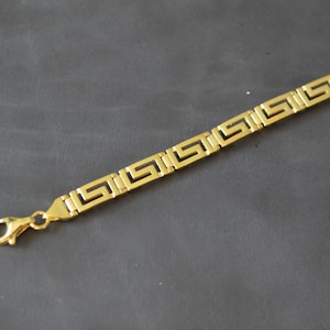 May include: A gold chain bracelet with a Greek key pattern.