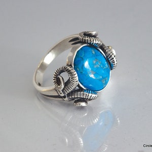 May include: A silver ring with a turquoise gemstone set in a design of stylized ram horns.