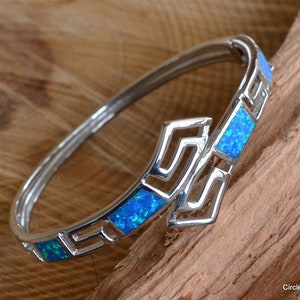 May include: Silver bangle bracelet with a Greek key design and blue opal stones.
