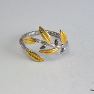 May include: A silver ring with a gold olive branch design. The ring is adjustable and has a delicate, minimalist style.