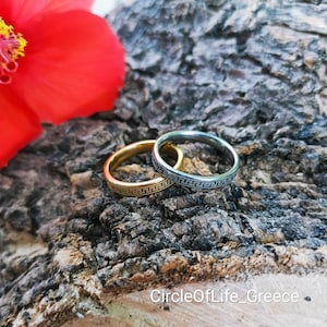 Può includere: Due semplici fasce con un design a chiave greca, una dorata e una argentata, su una superficie di legno.