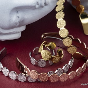May include: A set of three gold, silver, and rose gold bracelets with a unique design featuring a series of small, textured circles. The bracelets are arranged on a red surface.