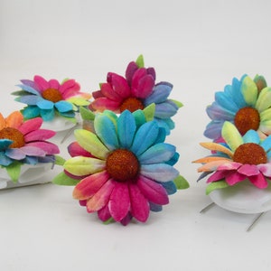 May include: Six colourful rainbow tie-dye paper flowers with glitter centres. The flowers are attached to white clips.