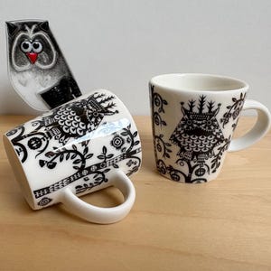 Peut inclure: Deux tasses en céramique blanche avec des motifs de hiboux noirs et une pièce décorative en forme de hibou assortie. Les tasses présentent une illustration de hibou noir et blanc et des motifs floraux.