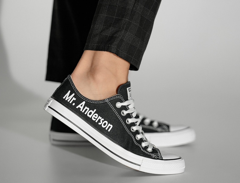 May include: Black canvas sneakers with white laces and a white sole. The left shoe has the text "Mr. Anderson" written on the side.