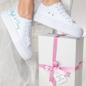 Pu&ograve; includere: Sneakers bianche in tela con un messaggio ricamato in verde che dice "Steph & Tony". Le sneakers sono legate con un nastro di raso bianco e sono appoggiate su una scatola regalo bianca con un nastro rosa e un'etichetta che dice "Made for your special day".