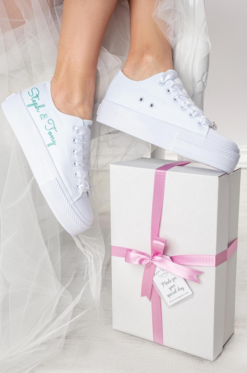 Pu&ograve; includere: Sneakers bianche in tela con un messaggio ricamato in verde che dice "Steph & Tony". Le sneakers sono legate con un nastro di raso bianco e sono appoggiate su una scatola regalo bianca con un nastro rosa e un'etichetta che dice "Made for your special day".