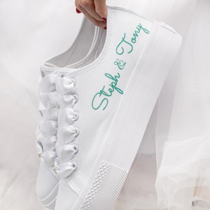 Pu&ograve; includere: Sneakers bianche in tela con lacci in nastro di raso bianco e il testo "Steph & Tony" ricamato in verde.