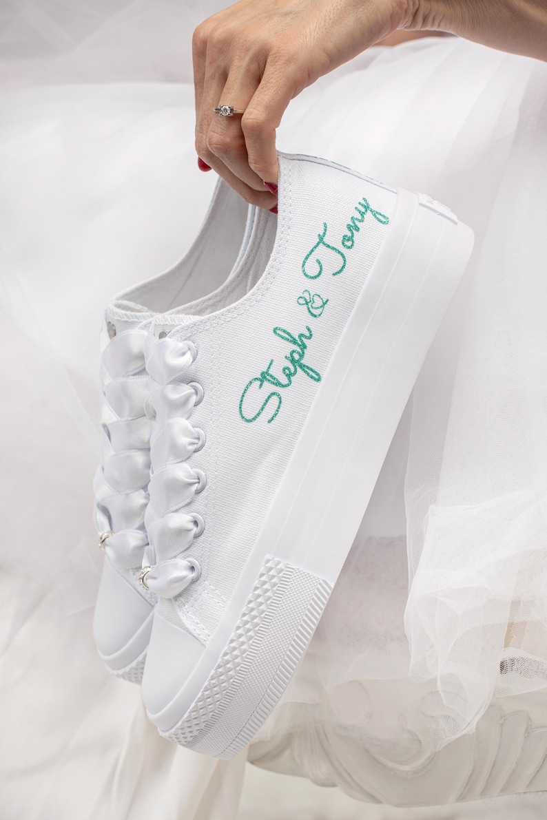 Pu&ograve; includere: Sneakers bianche in tela con lacci in nastro di raso bianco e il testo "Steph & Tony" ricamato in verde.