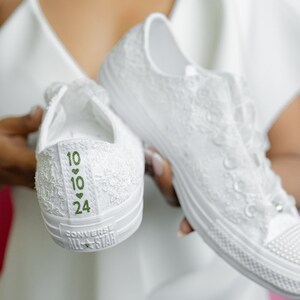 May include: White lace Converse All Star trainers with green numbers and hearts on the back. The numbers are 10, 10, and 24.