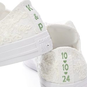 May include: White lace Converse sneakers with green embroidery. The left shoe has "K & P" embroidered on the back, and the right shoe has "10 &hearts; 10 &hearts; 24" embroidered on the back.