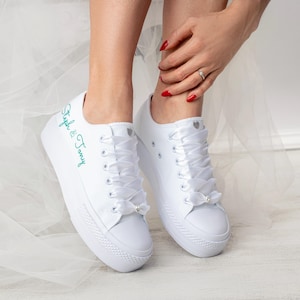 Pu&ograve; includere: Sneakers bianche in tela con lacci in raso bianco e un'iscrizione ricamata turchese che recita "Stephanie & Tommy".