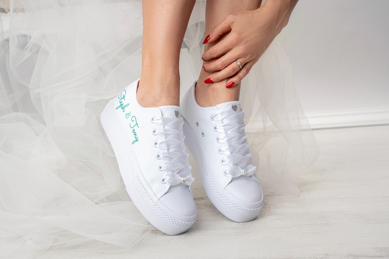 Pu&ograve; includere: Sneakers bianche in tela con lacci in raso bianco e un'iscrizione ricamata turchese che recita "Stephanie & Tommy".