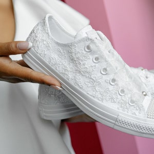 May include: White lace Converse trainers with pearl embellishments. The trainers have a white satin ribbon tied around the ankle.