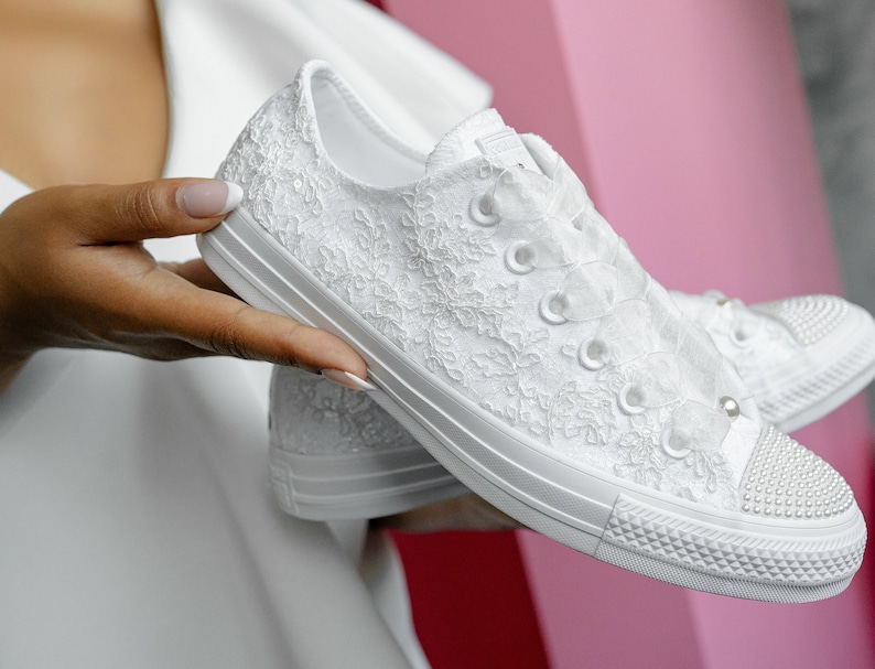 May include: White lace Converse trainers with pearl embellishments. The trainers have a white satin ribbon tied around the ankle.