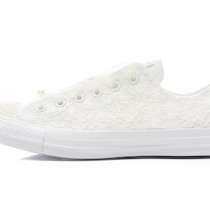 May include: White lace Converse sneakers with a pearl embellishment on the toe.