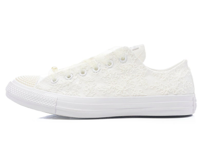 May include: White lace Converse sneakers with a pearl embellishment on the toe.