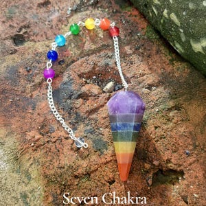 May include: A seven chakra pendulum with a faceted, cone-shaped crystal in shades of purple, blue, green, yellow, orange, and red. A silver chain connects the crystal to a strand of colorful beads. The text "Seven Chakra" is at the bottom.
