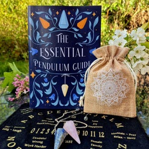 May include: A collection of divination tools, including a book titled "The Essential Pendulum Guide", a burlap drawstring bag with a white mandala design, and a pendulum with blue and pink crystal points. A black surface with numbers and letters is also visible.