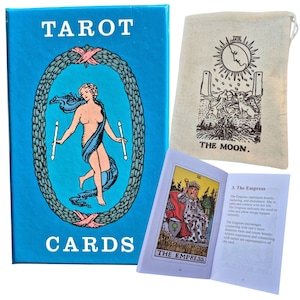 May include: A blue tarot card box with the text TAROT CARDS, a beige drawstring pouch featuring a black illustration of The Moon card, and an open guidebook displaying The Empress card with descriptive text on the adjacent page.