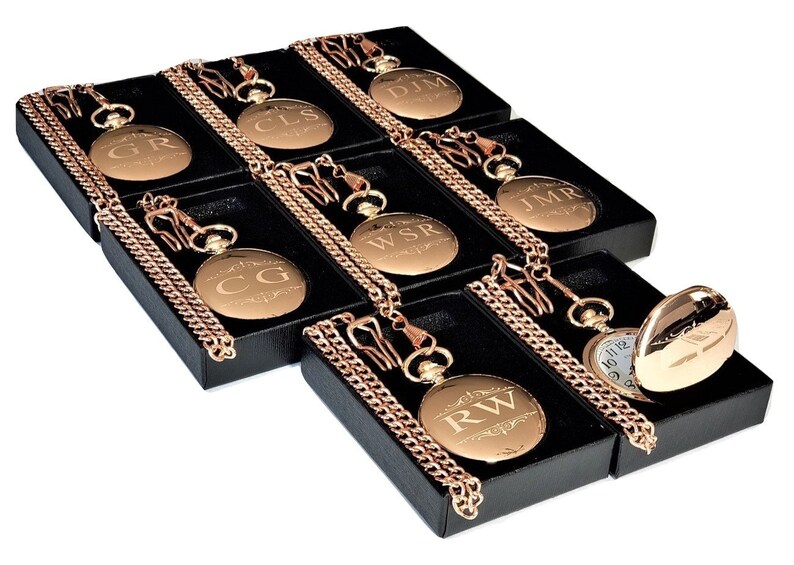 Puede incluir: Ocho relojes de bolsillo de oro con cadenas en cajas negras. Cada reloj tiene un monograma grabado diferente en la parte delantera. Los relojes est&aacute;n dispuestos en un patr&oacute;n escalonado.