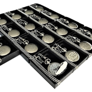 Puede incluir: Una muestra de relojes de bolsillo plateados con cadenas en cajas de terciopelo negro. Cada reloj tiene una inscripci&oacute;n grabada.