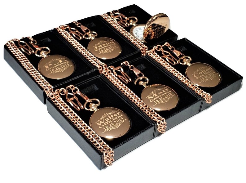 Puede incluir: Seis relojes de bolsillo dorados con cadenas en cajas negras. Cada reloj tiene una inscripci&oacute;n personalizada con un nombre y la fecha "10.26.2019".