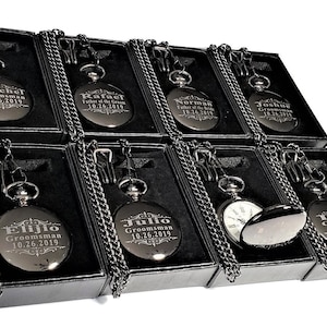 May include: Eight black pocket watches with chains in black boxes. Each watch has a different name engraved on it, such as "Mitch,  Groomman 10.26.2019".