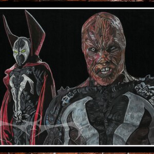 May include: A framed artwork featuring two figures from the Spawn comic series. One figure is in a black and white costume with a red cape and hood. The other figure has a scarred face and a dark costume.