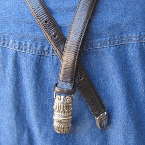 May include: A brown leather belt with a silver buckle. The buckle is ornate and has a geometric design.