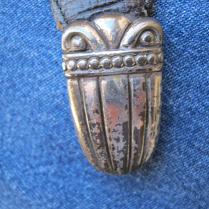 May include: Close-up of a silver-toned metal sword pommel with a decorative design. The pommel has a rounded top and a fluted body.