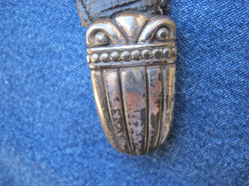 May include: Close-up of a silver-toned metal sword pommel with a decorative design. The pommel has a rounded top and a fluted body.