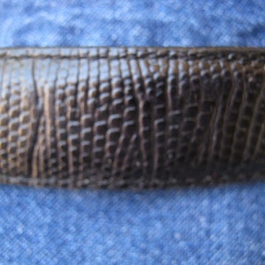 May include: Close-up of a dark brown leather belt with a textured, alligator-like pattern.