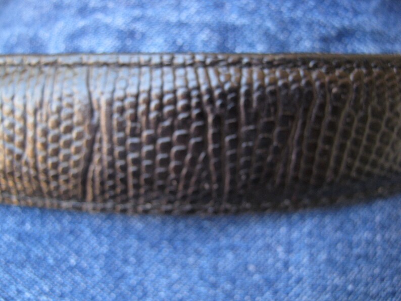 May include: Close-up of a dark brown leather belt with a textured, alligator-like pattern.