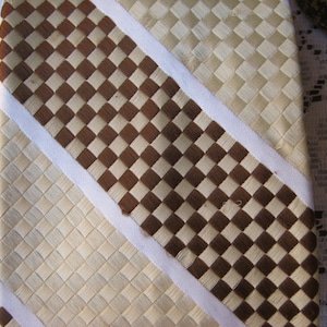 May include: A woven tie with a brown and white checkered pattern and white stripes. The tie is made of a natural material, possibly straw or bamboo.
