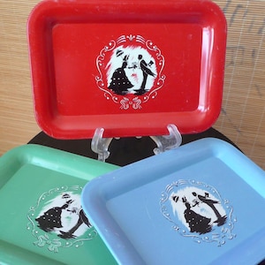 Puede incluir: Tres bandejas de servir de metal con un diseño vintage. Las bandejas son rojas, verdes y azules. Cada bandeja presenta una silueta de una pareja bailando con un borde decorativo.