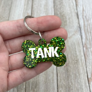 May include: Green glitter dog bone tag with the name "TANK" in white letters.