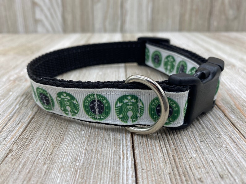 May include: A white and green dog collar with a repeating pattern of the Starbucks logo. The collar has a black adjustable buckle and a silver D-ring.