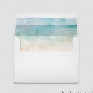 May include: A white envelope with a watercolor design of a beach scene on the inside flap. The design features shades of blue and green for the ocean and sky, and a light brown for the sand.