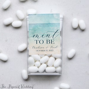 May include: Mint to be wedding favor boxes with a watercolor design and the text "mint to be" in cursive. The boxes are filled with white mints and have a label that says "Madison & Nick" and "October 15, 2025".