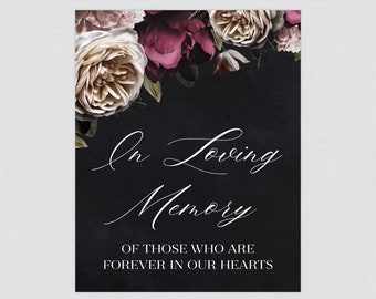 May include: A memorial sign with a dark background and floral arrangement at the top. The sign reads "In Loving Memory" in elegant script, followed by "Of those who are forever in our hearts."