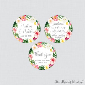 May include: Three round wedding favor stickers with a tropical floral design. The stickers feature the text "Madison & Nicholas" and the date "July 25, 2025". One sticker says "A Sweet Ending to our new beginning", another says "Madison & Nicholas" and the third says "Thank You".