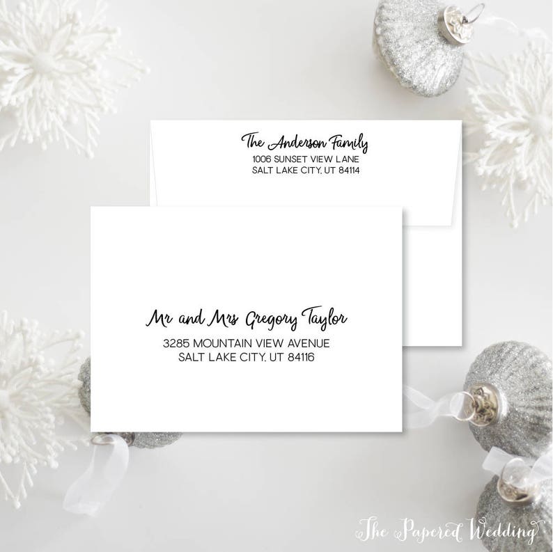 May include: White envelopes with black calligraphy text. One envelope reads "The Anderson Family" with an address. The other envelope reads "Mr and Mrs Gregory Taylor" with an address. Decorative silver ornaments and white floral accents are in the background.