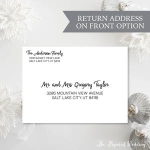 May include: A white envelope with black text featuring the names "The Anderson Family" and "Mr and Mrs Gregory Taylor" with their addresses. The text "RETURN ADDRESS ON FRONT OPTION" is above the envelope. Decorative silver ornaments and white floral accents are in the background.