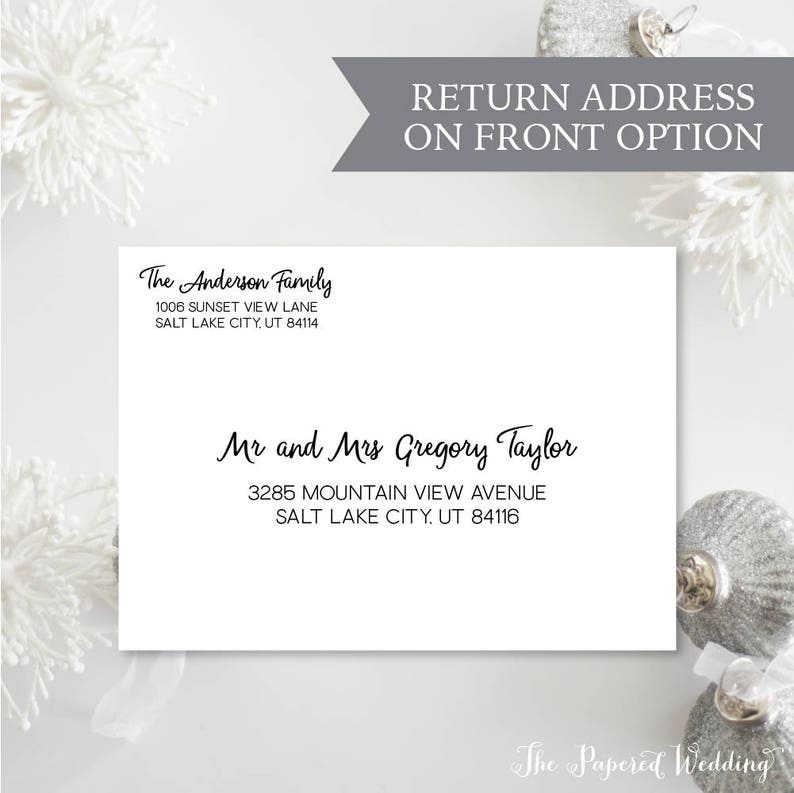 May include: A white envelope with black text featuring the names "The Anderson Family" and "Mr and Mrs Gregory Taylor" with their addresses. The text "RETURN ADDRESS ON FRONT OPTION" is above the envelope. Decorative silver ornaments and white floral accents are in the background.